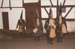 Eine Gruppe dunkel gekleideter Belzemärtel, mit spitzem Hut, vermummten Gesichtern, Bärten aus Hanf und Rute