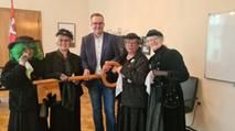 4 schwarz gekleidete Damen geben den großen Holzschlüssel an den Bürgermeister-Vertreter zurück