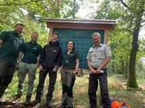 Fünf Mitarbeitende des Forstamts vor beschriebener Tafel im Waldklassenzimmer