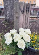 Gedenksteine in Form eines Floßes, davor weiße Rosen 