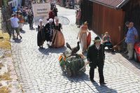 Ein Jäger fährt einen ausgestopften Auerhahn im Leiterwagen, dahinter Personen in adeliger Kleidung