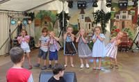 Kinder in kurzen Hosen und Kleidhcen tanzen auf der Bühne