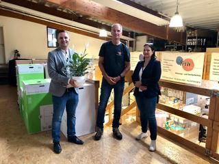 Zwei Männer und eine Frau bei Jubiläumsgeschenkübergabe im Handwerksbetrieb.