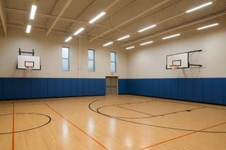 Die Realschulhalle erhält eine energiesparende Beleuchtung. Eine leere Sporthalle mit Basketballkörben und Energiesparbeleuchtung