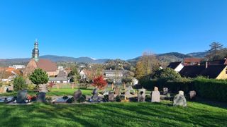 Friedhof, Blick auf Gräber und Grabsteine von hinten und auf die Kirche