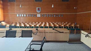 Stühle, Rednerplätze, Tische in einem Sitzungssaal, ein Wappen an der Wand