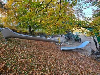 Bauarbeiten Spielplatz Scheuern. Laub im Vordergrund, eine Kinderrutsche, Baufahrzeug