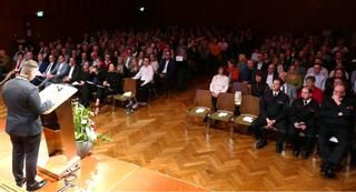 Redner von hinten auf der Bühne, Blick ins Publikum 