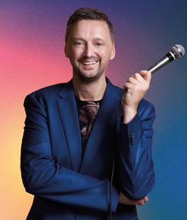 Ein Mann hält lachend ein Mikrofon von sich weg. 