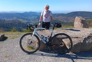 Ein Mann im Radtrikot, ein Rennrad, vor grandiosem Ausblick 