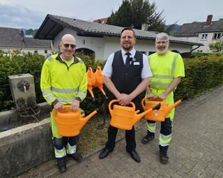 Stefan Merli bei der Übergabe der Gießkannen an den Bauhof. Stefan Merli, rechts und links Bauhofmitarbeiter, jeder mit Gießkanne in der Hand.