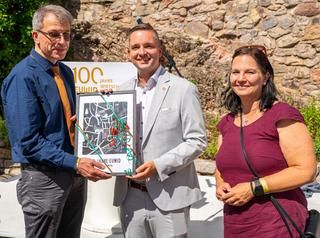 Dr. Martin Katz, Bürgermeister Julian Christ und Wirtschaftsförderin Nicoletta Arand. 2 Herren halten ein Plakat hoch, daneben steht eine Dame.