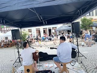 Vorne zwei Männer mit Gitarre, Hintergrund unscharf.