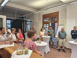 Frauen und Männer in einem Raum beim Hören der Begrüßung