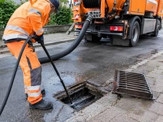 Ein Mann in Arbeitsmontur saugt einen Straßenablauf. 