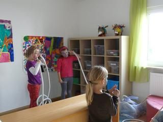 3 Kinder mit bemalten Gesichtern blasen in Röhren.