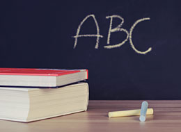 Die Buchstaben ABC mit Kreide auf eine Tafel geschrieben, zwei Bücher aufeinandergestapelt