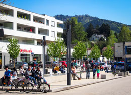 Menschen sitzen, laufen, stehen am Salmenplatz. Im Hintergrund das Mehrfamilienhaus mit.