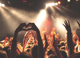 Konzertbesucher lauschen einer Live-Band und jubeln mit den Armen nach oben