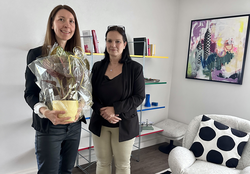 Wirtschaftsförderin Nicoletta Arand (re) gratuliert Lia Skopnik (li) zur Neueröffnung. Links Frau mit Pflanze daneben andere Frau rechts ein buntes Bild an der Wand und ein getupftes Kissen in einem weißen Sessel.