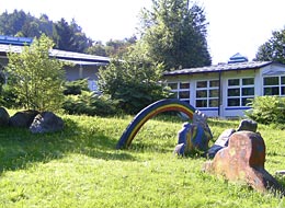 Außenbereich des evangelischen Kindergarten Scheuern, mit einer Wiese und einem Regenbogen aus Holz.