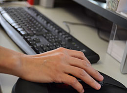 Eine Hand bedient die Computermaus, im Hintergrund die Tastatur