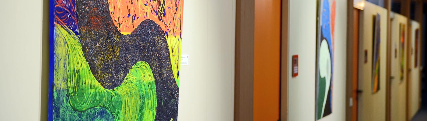 Bei einer Kunstausstellung im Rathaus hängen farbenfrohe Gemälde an den Wänden des Rathausflures