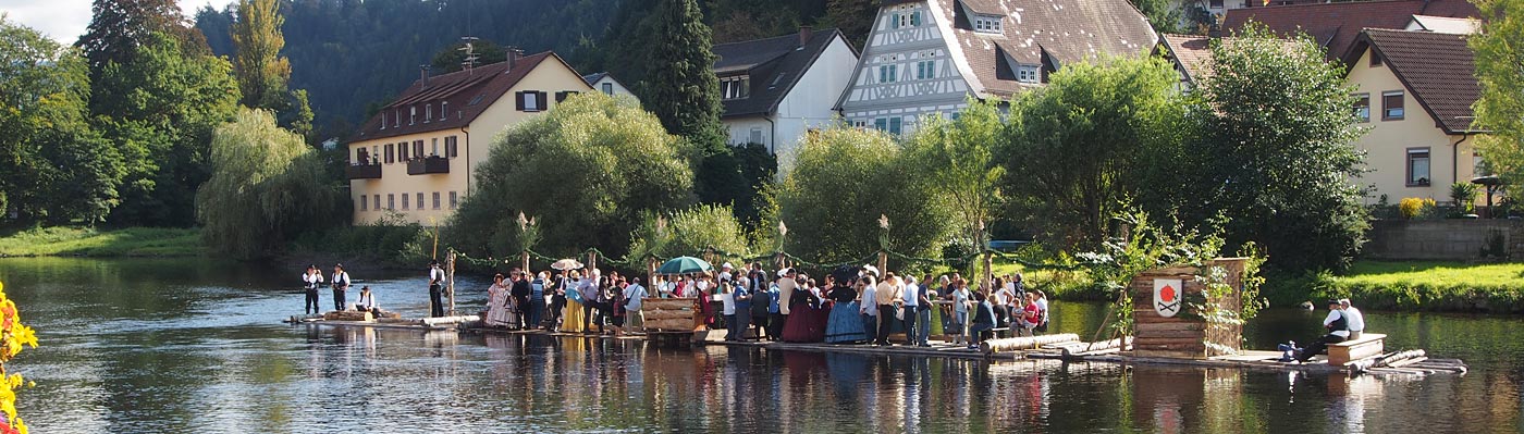 Das Floß in der Murg mit einer Gruppe von Menschen bei einer Floßfahrt vor der Altstadtkulisse von Gernsbach