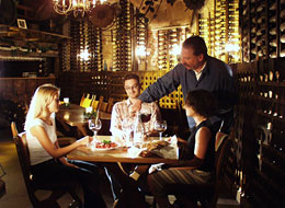 Weinprobe im Weinkeller des Alten Rathauses Drei Personen sitzen am Tisch bei Kerzenlicht und lassen sich Wein einschenken