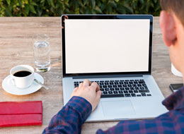 Person sitzt am Laptop mit Wasserglas und Kaffeetasse