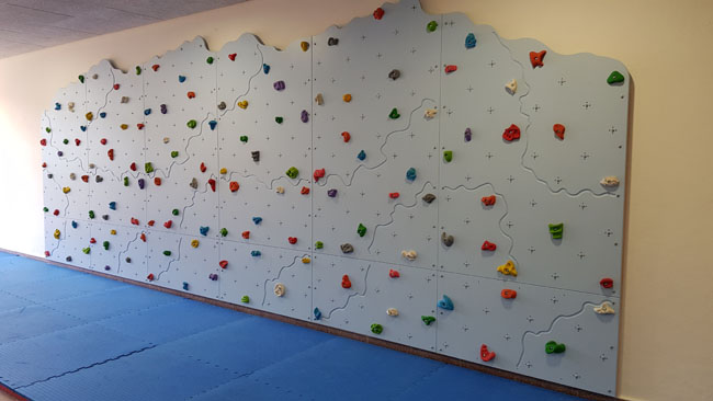 Vor der Kletterwand mit bunten Griffen liegen blaue Matten