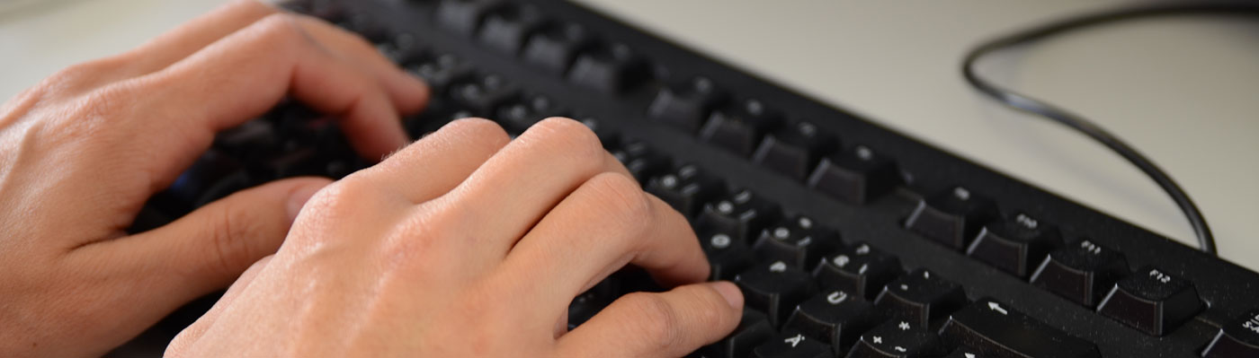 Hände schreiben auf einer schwarzen Computer-Tastatur