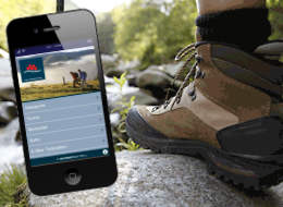 Ein Mobiltelefon mit der SchwarzwaldApp neben einem Wanderschuh