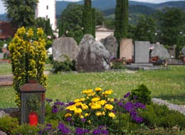 Friedhof mit blumengeschmückten Gräbern und Grabsteinen im Hintergrund