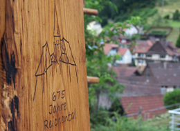 Logo 675 Jahre Reichental in Holz gebrannt, im Hintergrund Häuser in Reichental