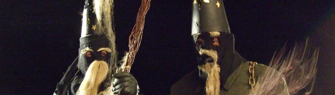 Zwei dunkel gekleideten Belzemärtel, mit spitzem Hut, vermummten Gesichtern, Bärten aus Hanf und Rute