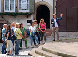 Eine Gruppe von Menschen bei einer Stadtführung vor dem Alten Rathaus. Die Stadtführerin erklärt das Gebäude.