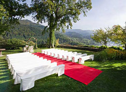 Festbänke mit weißen Hussen, im Mittelgang ein roter Teppich, der Trautisch unter einem Rosenbogen im Garten von Schloss Eberstein