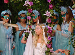 öffnet in neuem Fenster Internetseite Theater im Kurpark Titania auf einer Blütenschaukel umringt von ihren maskierten Elfen. Das Theater im Kurpark spielt "Ein Sommernachtstraum"