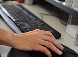 weiter zu den Online-Diensten Eine Hand bedient die Computermaus, im Hintergrund die Tastatur