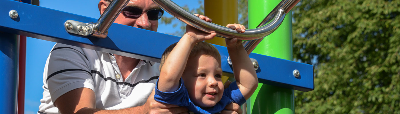 auf dem Spielplatz Kleiner Junge wird von Erwachsenem beim Einstieg einer Rutsche gehalten