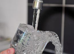 Überlaufendes Wasserglas unter einem aufgedrehten Wasserhahn