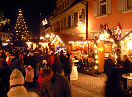weiter zum Weihnachtsmarkt Gernsbach Besucher zwischen weihnachtlich beleuchtete Hütten und Weihnachtsbaum beim Weihnachtsmarkt in der Altstadt