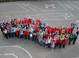Auf dem Schulhof stehen Schüler in einer Wellen-Formation und schauen nach oben zum Fotografen.