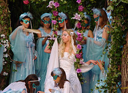 weiter zu Kulturveranstalter Titania auf einer Blütenschaukel umringt von ihren maskierten Elfen. Das Theater im Kurpark spielt "Ein Sommernachtstraum"