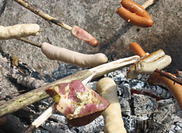 weiter zu den Grillplätzen verschiedene Würste an Stecken brutzeln über dem Lagerfeuer